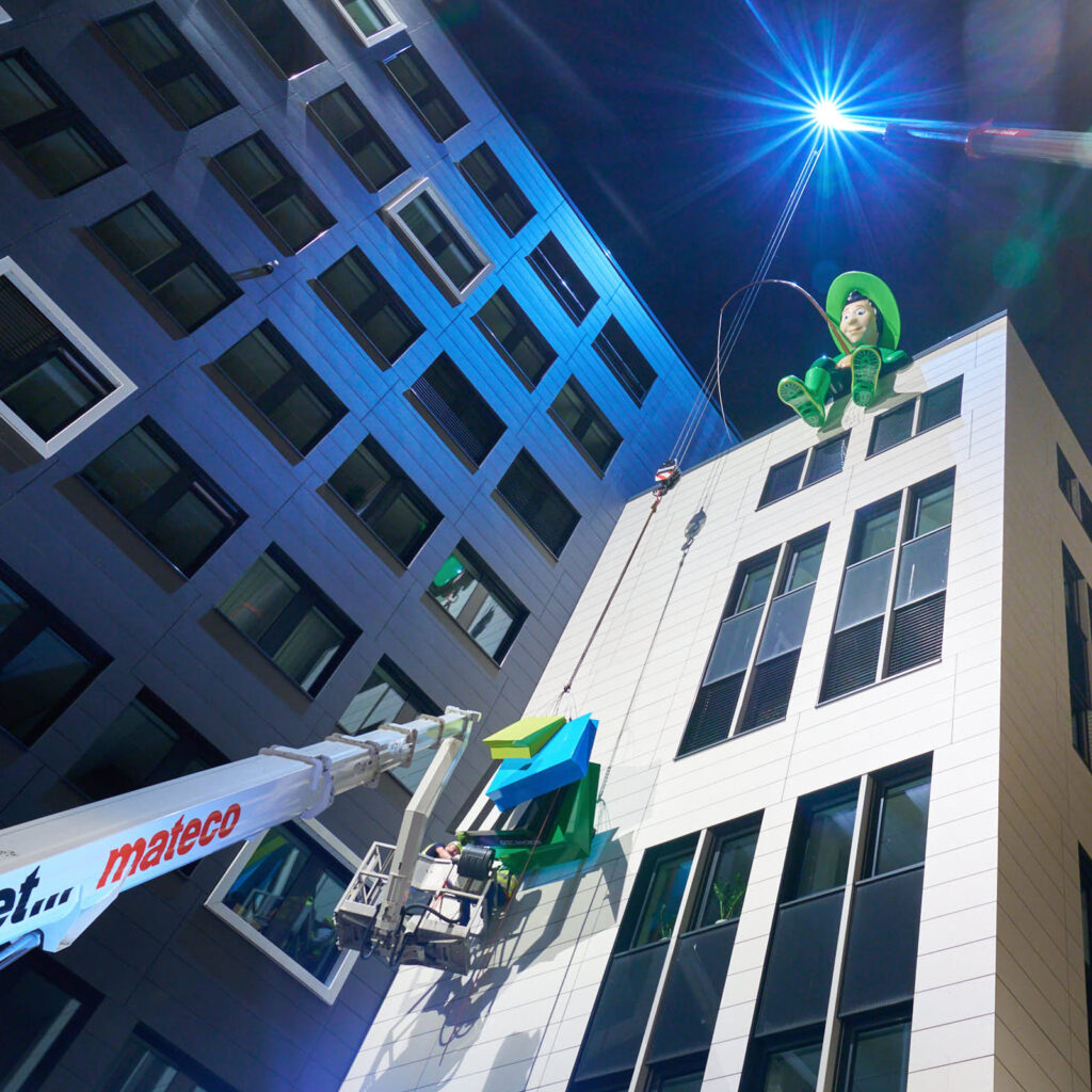 Der beleuchtete Konsum-Angler an der Fassade eines Gebäudes bei Nacht.